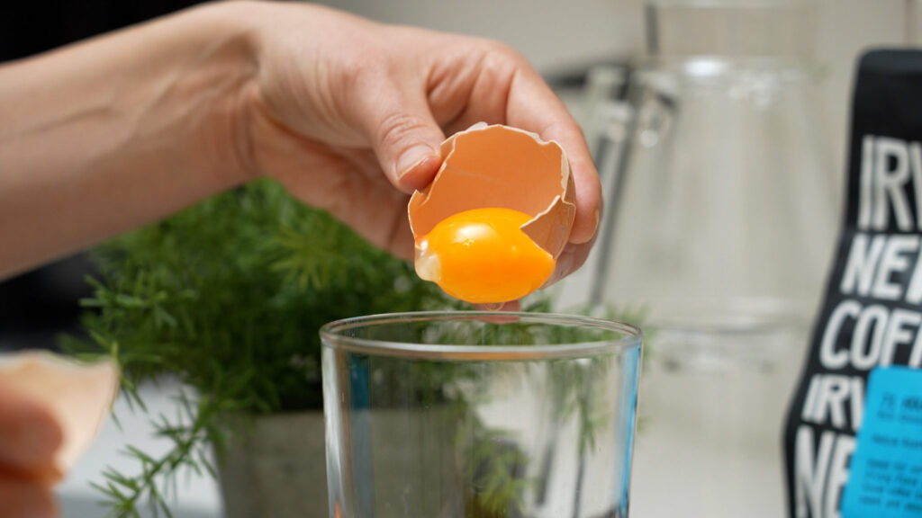 A barista whisking egg yolk and sugar in a glass, with tea being poured in